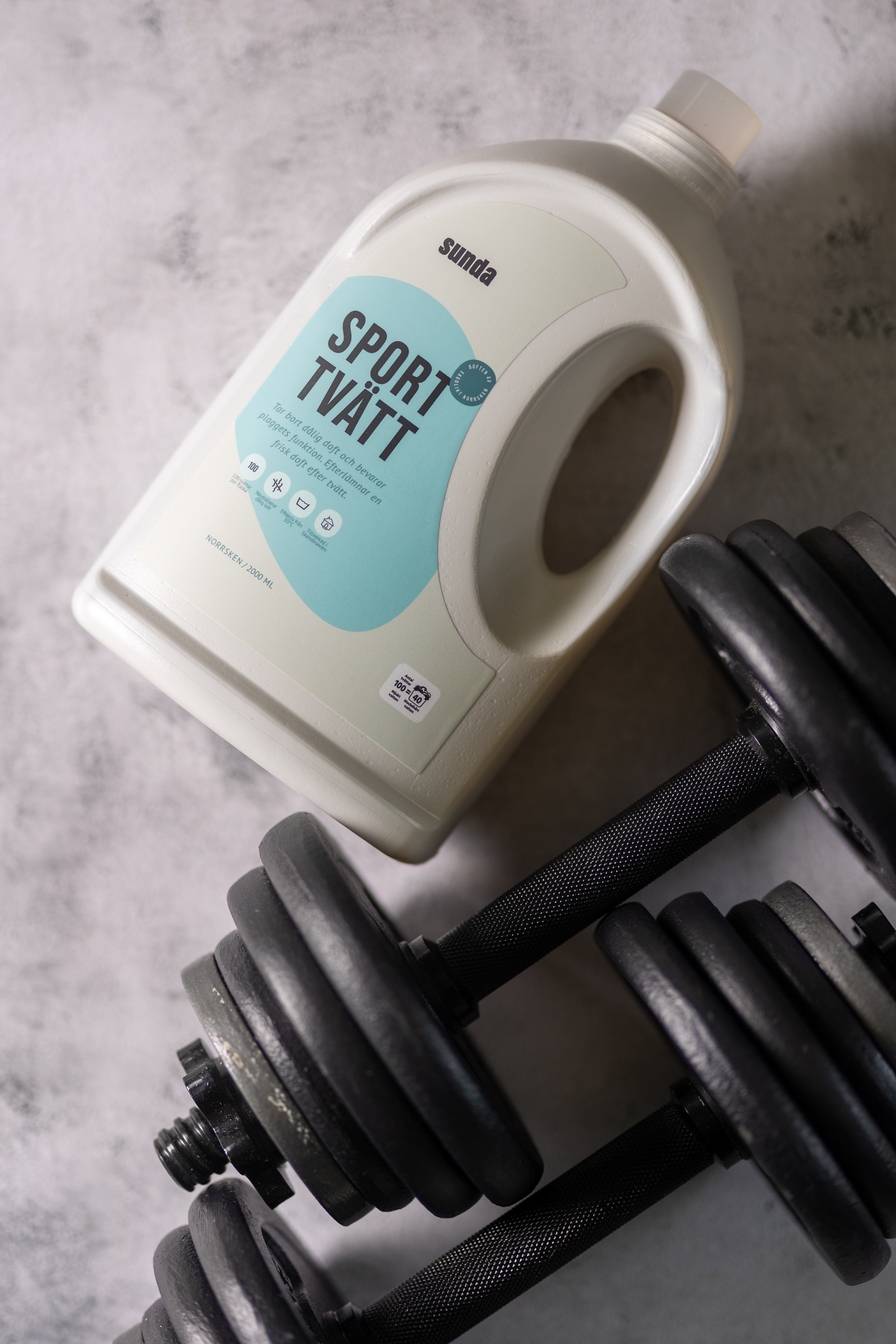 Laundry detergent bottle next to a pair of black dumbbells on a gray surface.