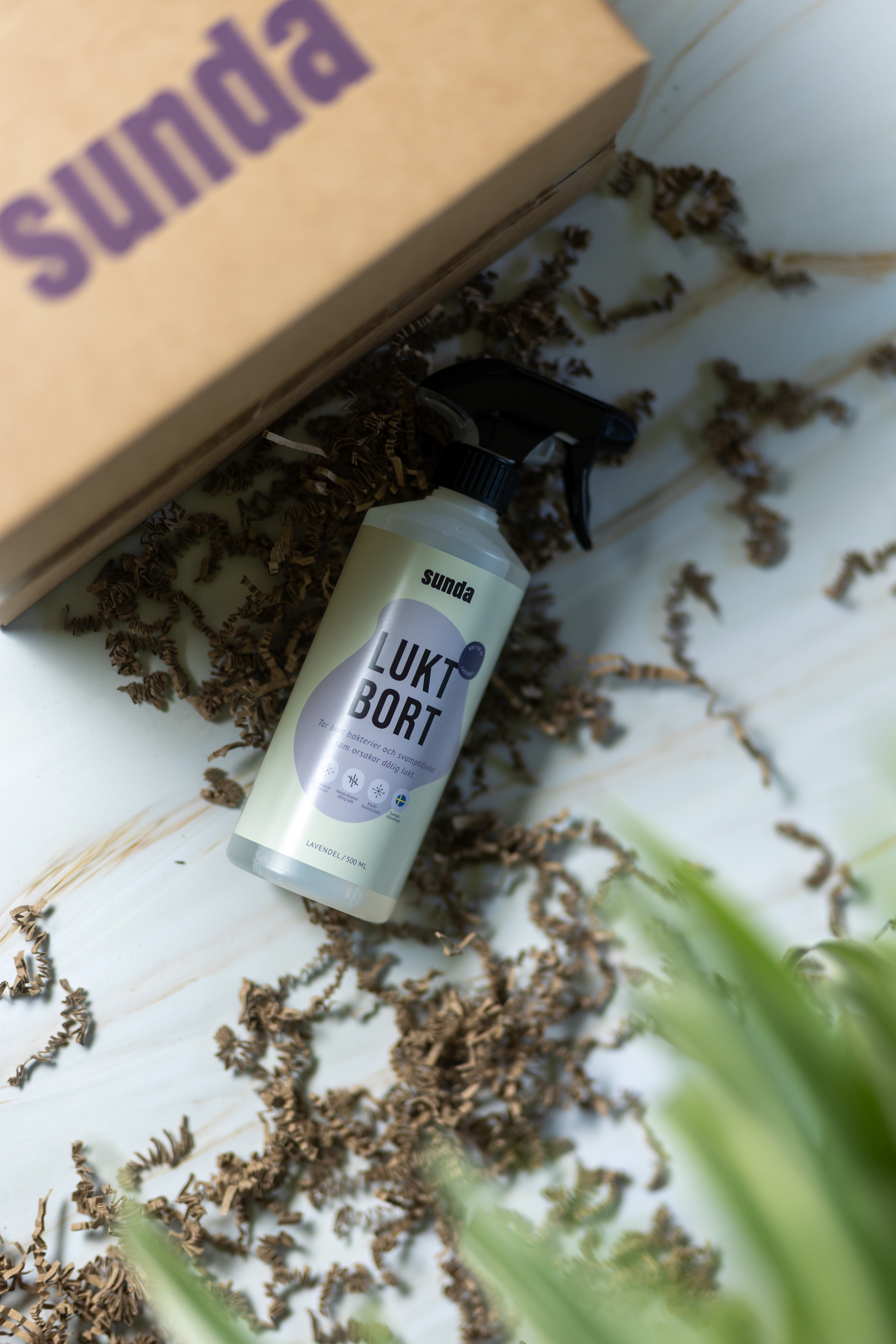 Spray bottle labeled 'Lukt Bort' on a table with shredded paper and a cardboard box.