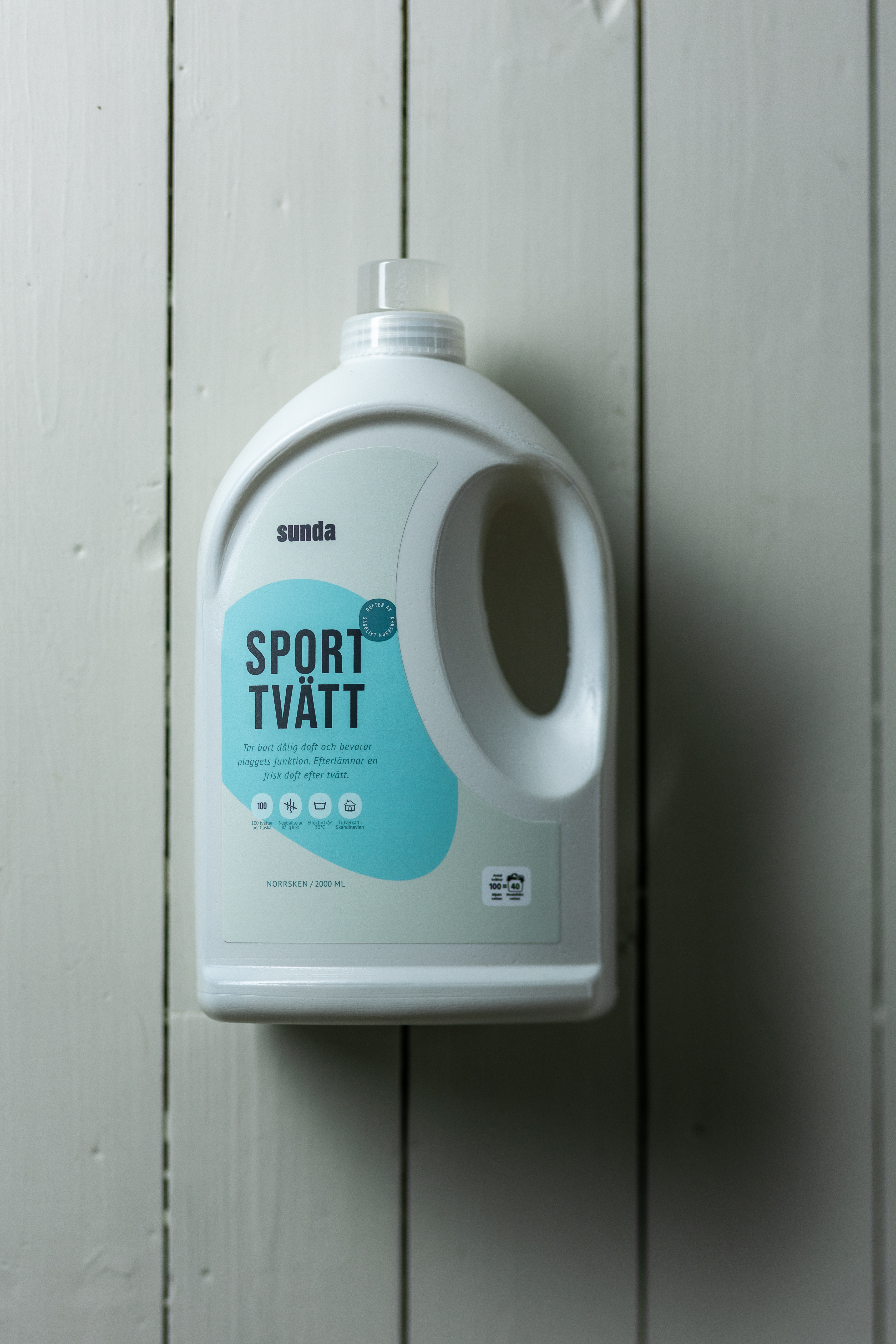 White bottle of laundry detergent labeled 'Sport Tvätt' on a wooden surface.
