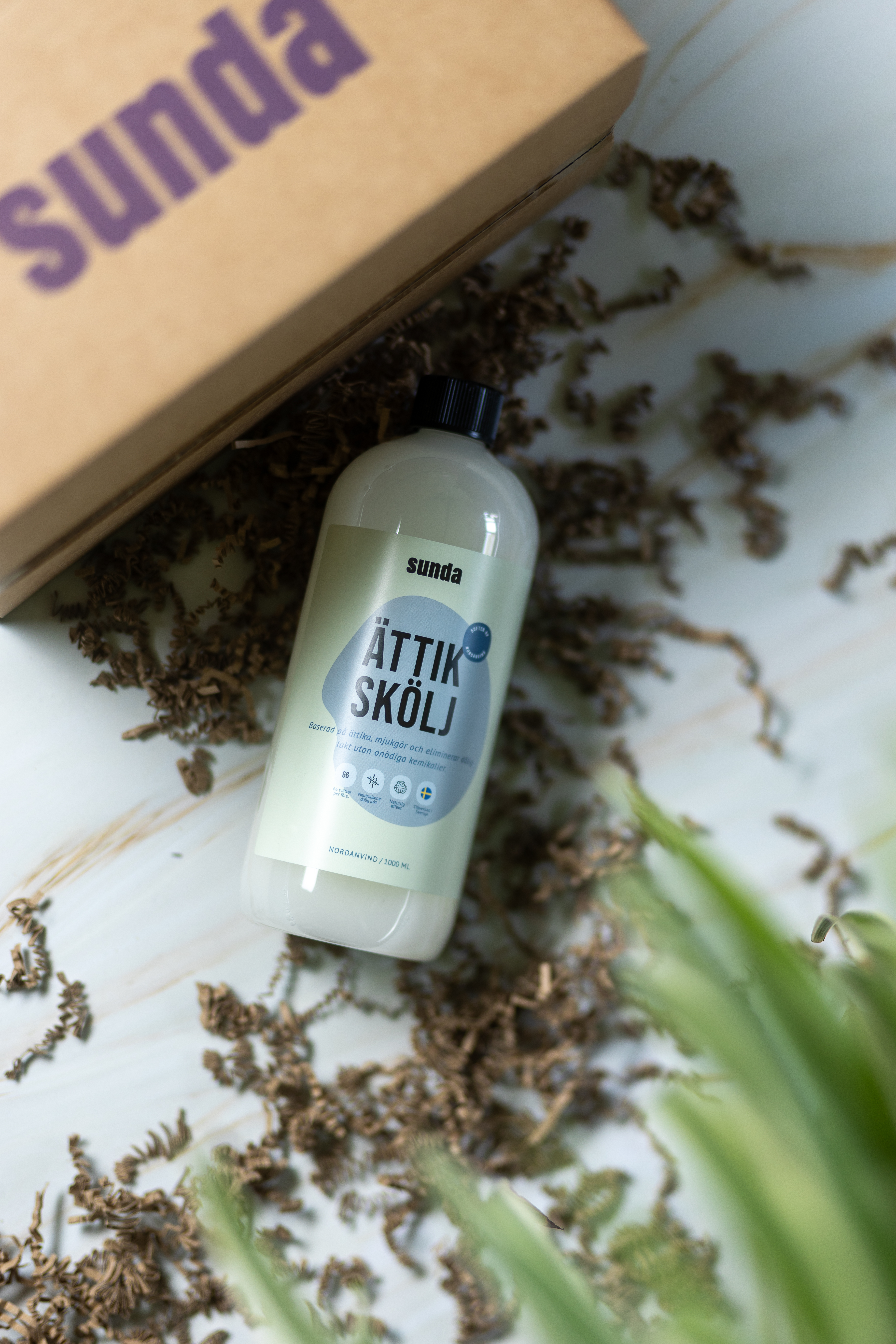 Bottle labeled 'Ättik Skölj' on a table with dried leaves and a box.