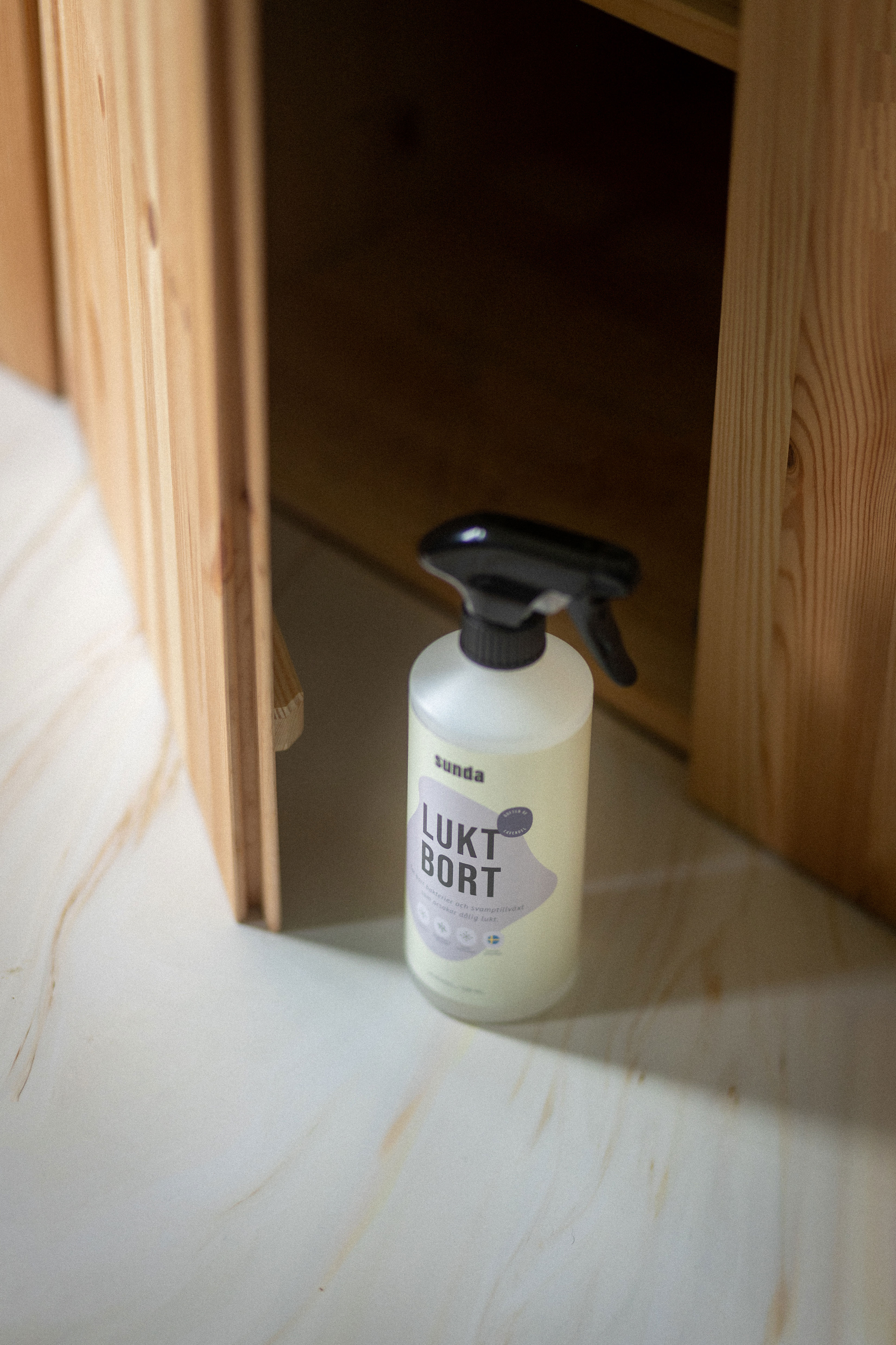 Spray bottle labeled 'Lukt Bort' on a light-colored surface near wooden cabinet.
