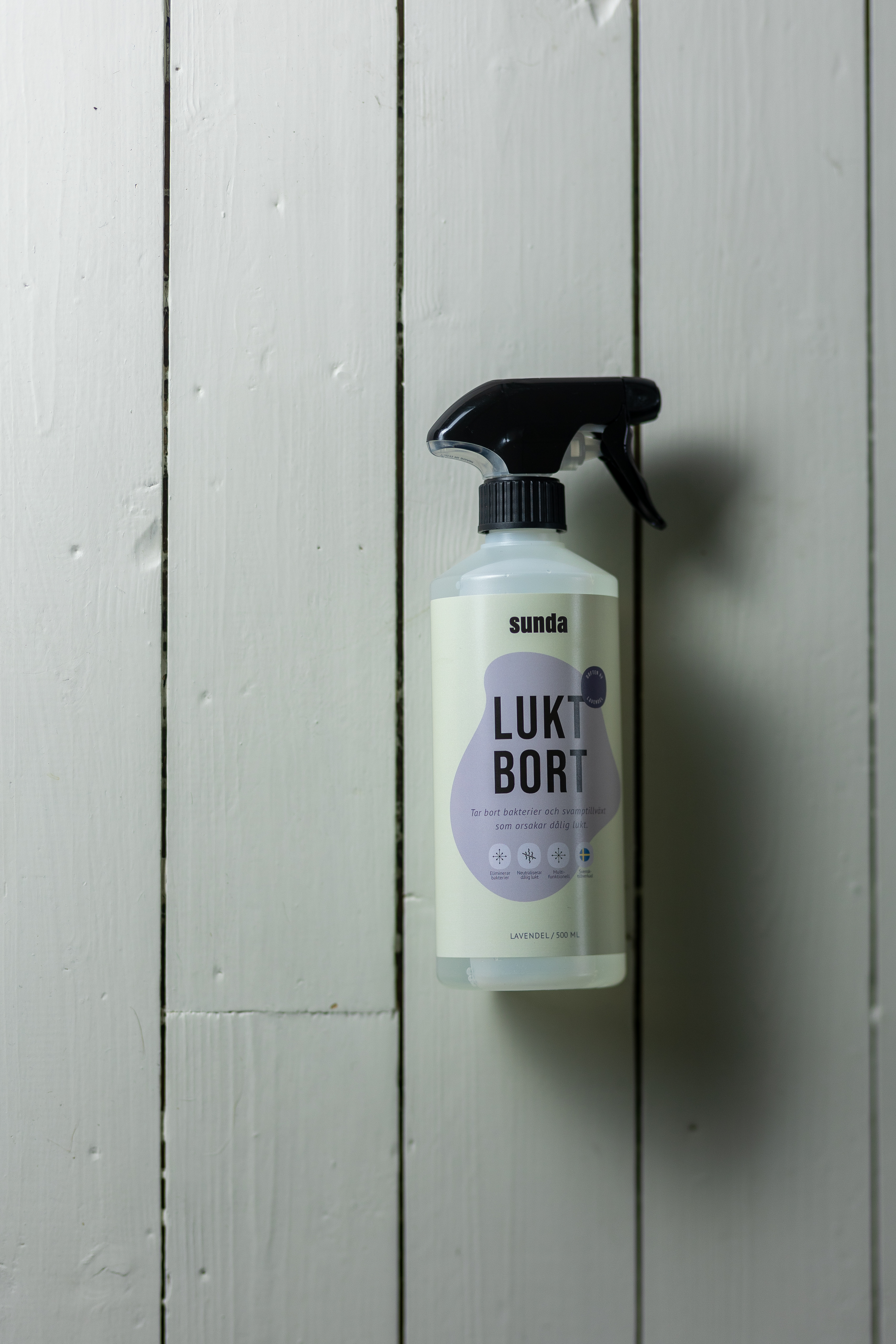 Spray bottle labeled 'Lukt Bort' against a white wooden background.
