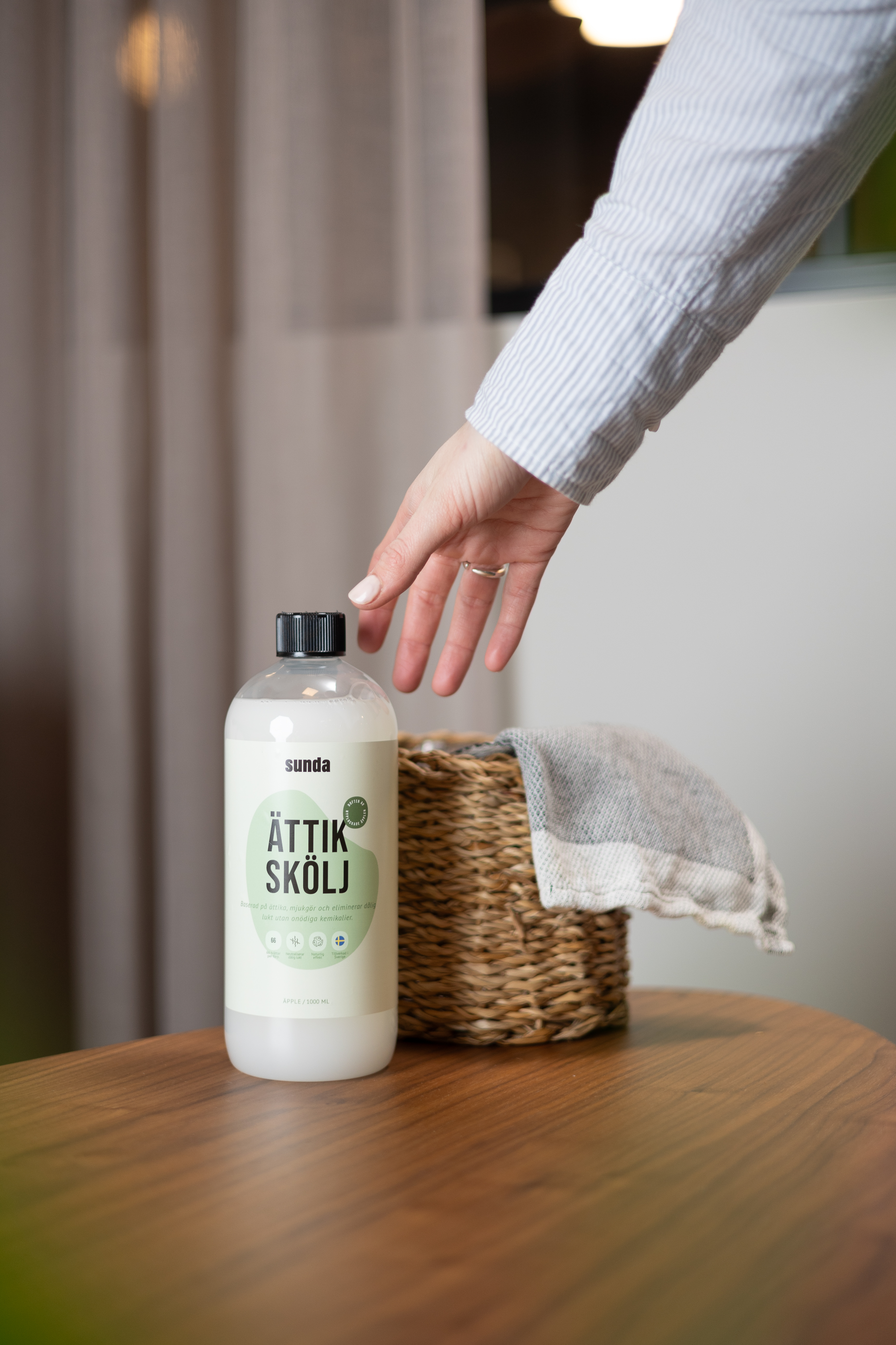 Hand reaching for a bottle labeled 'Ättik Skölj' on a wooden table.