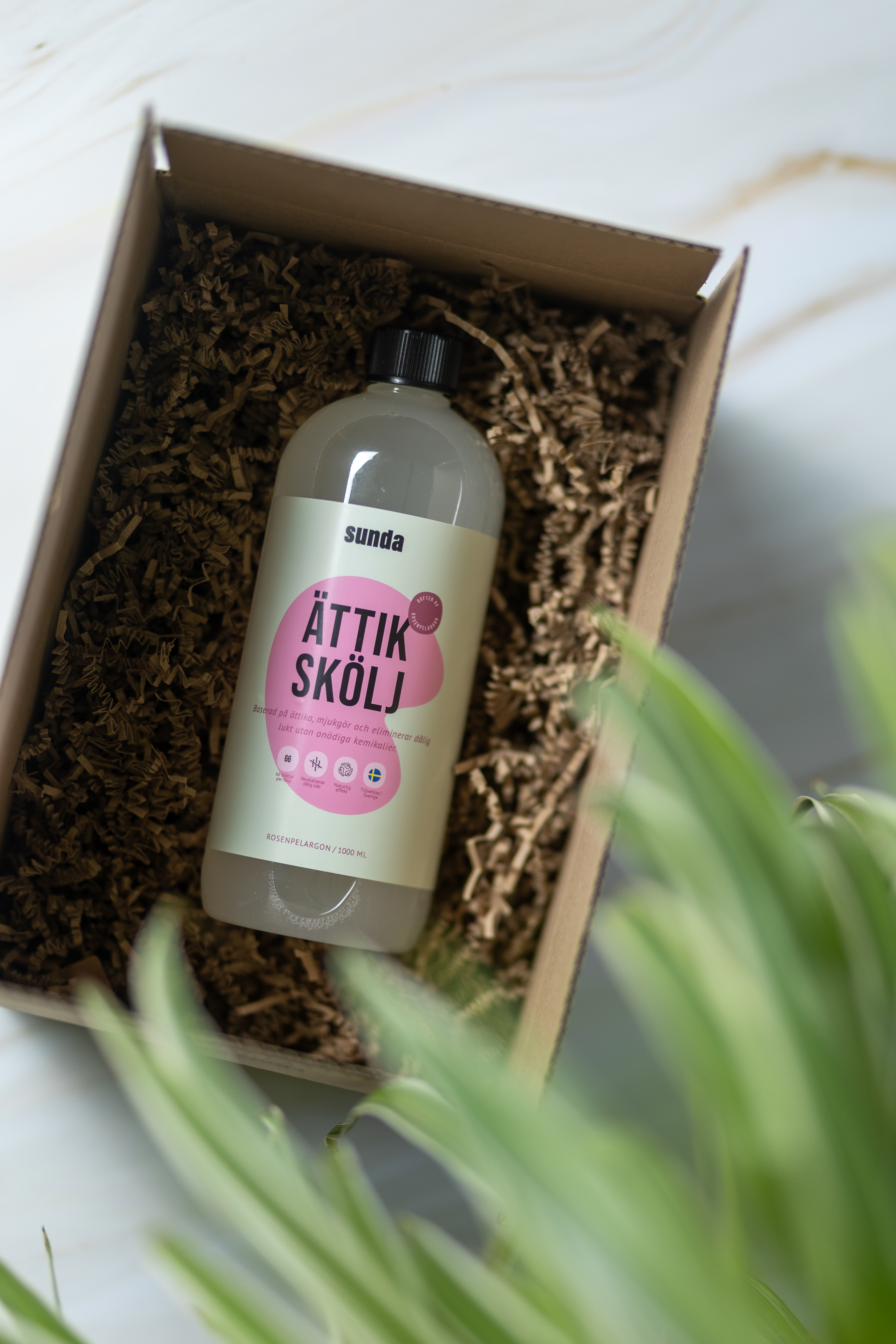 A bottle labeled 'Ättik Skölj' in a box with shredded paper.