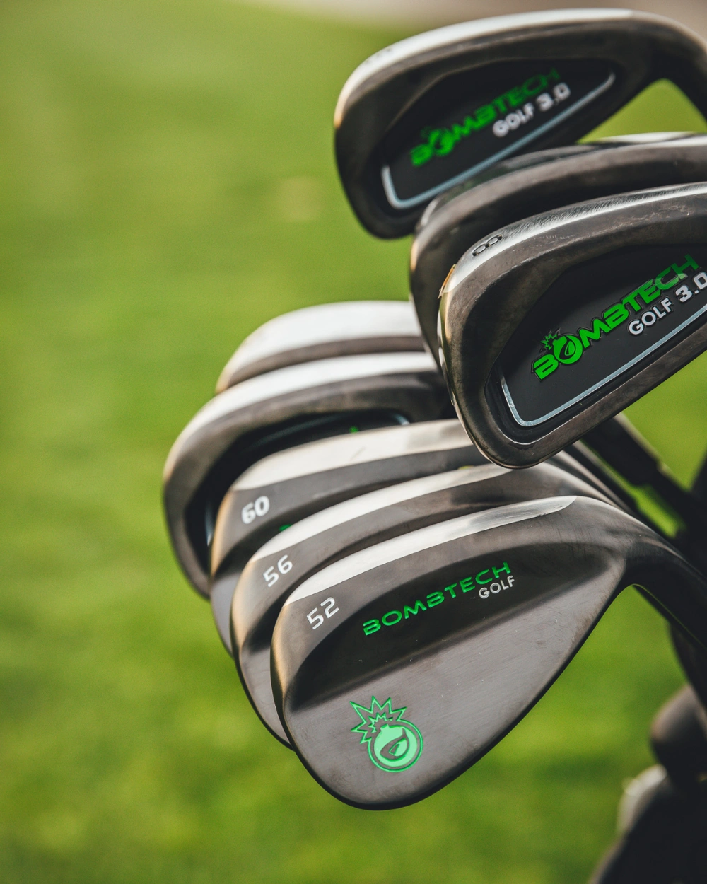 Set of BombTech golf clubs with green text on a grassy background.