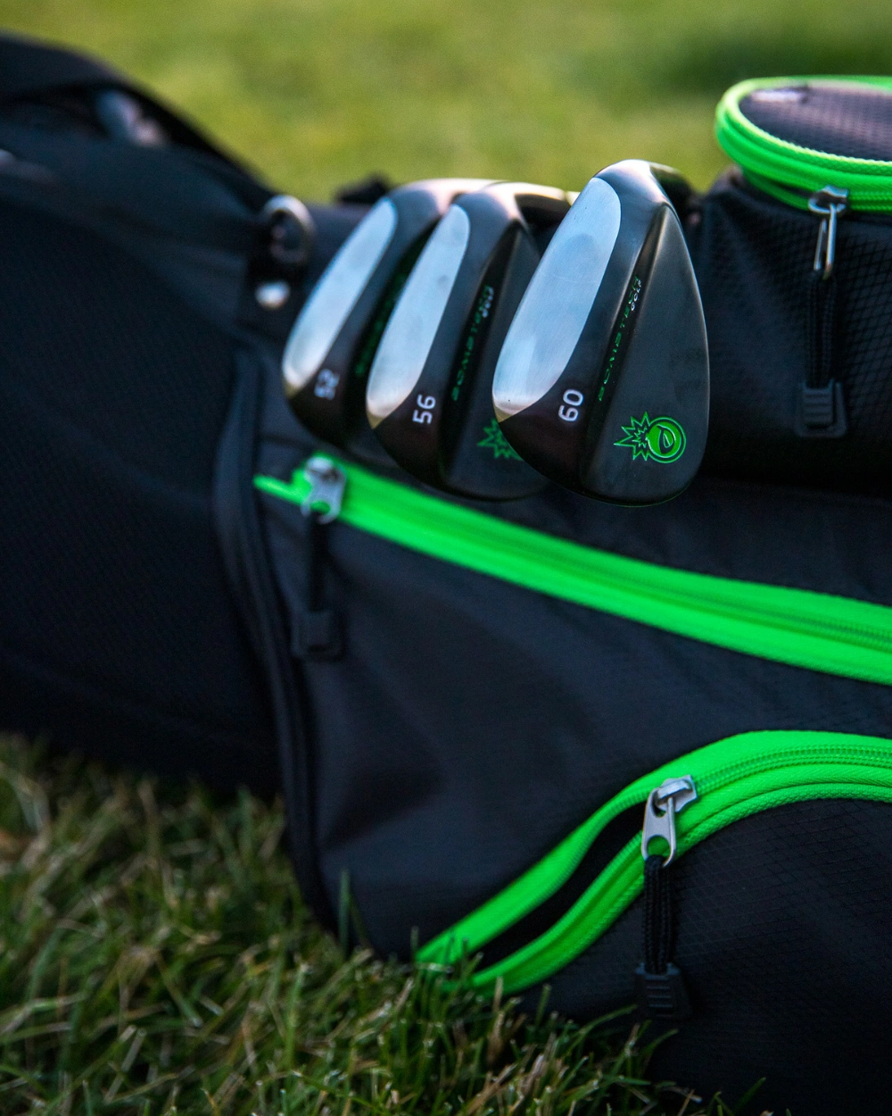Golf clubs in a bag with bright green zippers on grass.