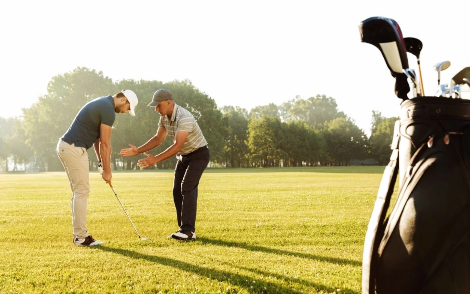Two people on a golf course, one instructing the other, with golf bag in foreground.