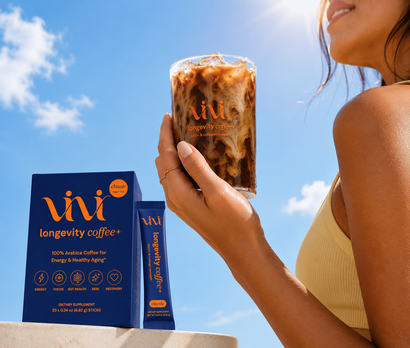 A person holds a glass of iced coffee next to a box and packet of Vivi Longevity Coffee+.