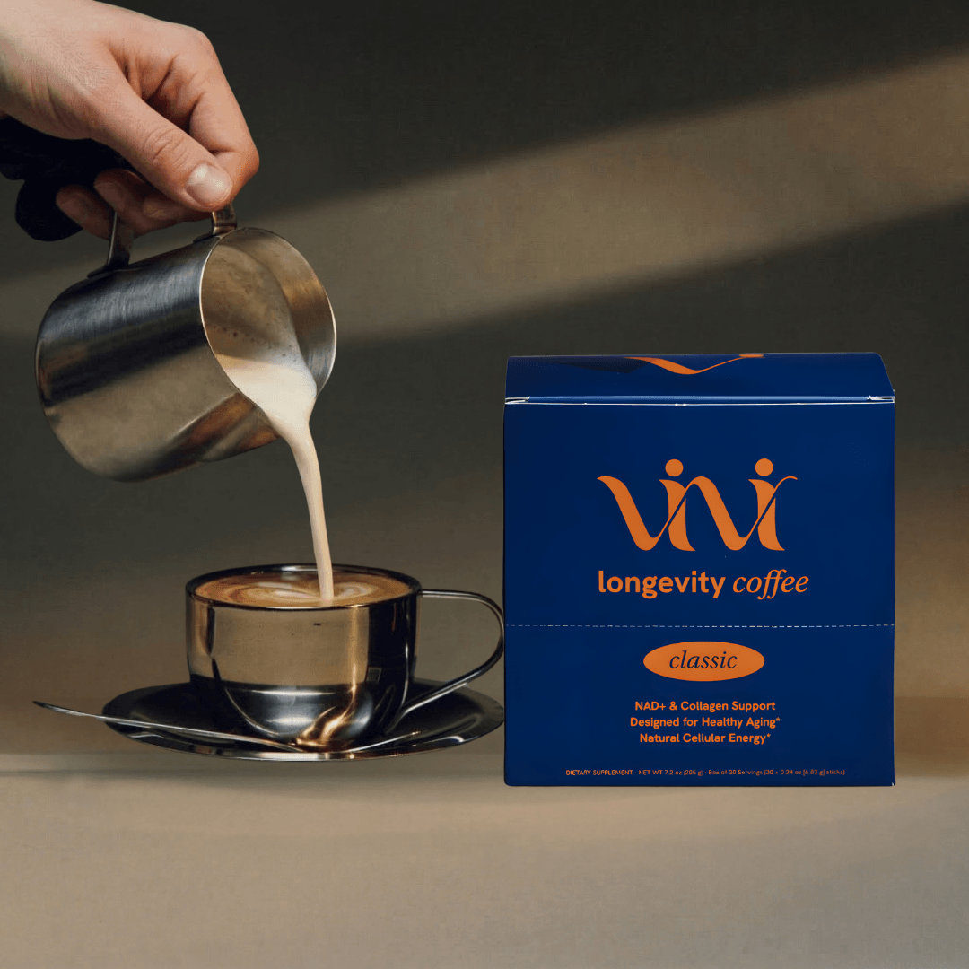 A hand pours steamed milk into a coffee cup next to a blue box of Vivi longevity coffee.