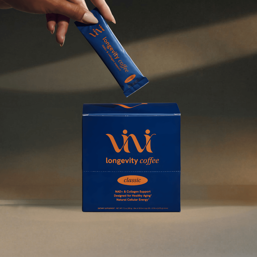 A hand holds a single-serving packet of ViVi longevity coffee above its blue and orange box.