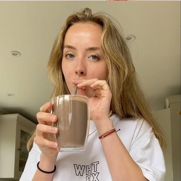 Person drinking a beverage from a glass with a straw in a kitchen.