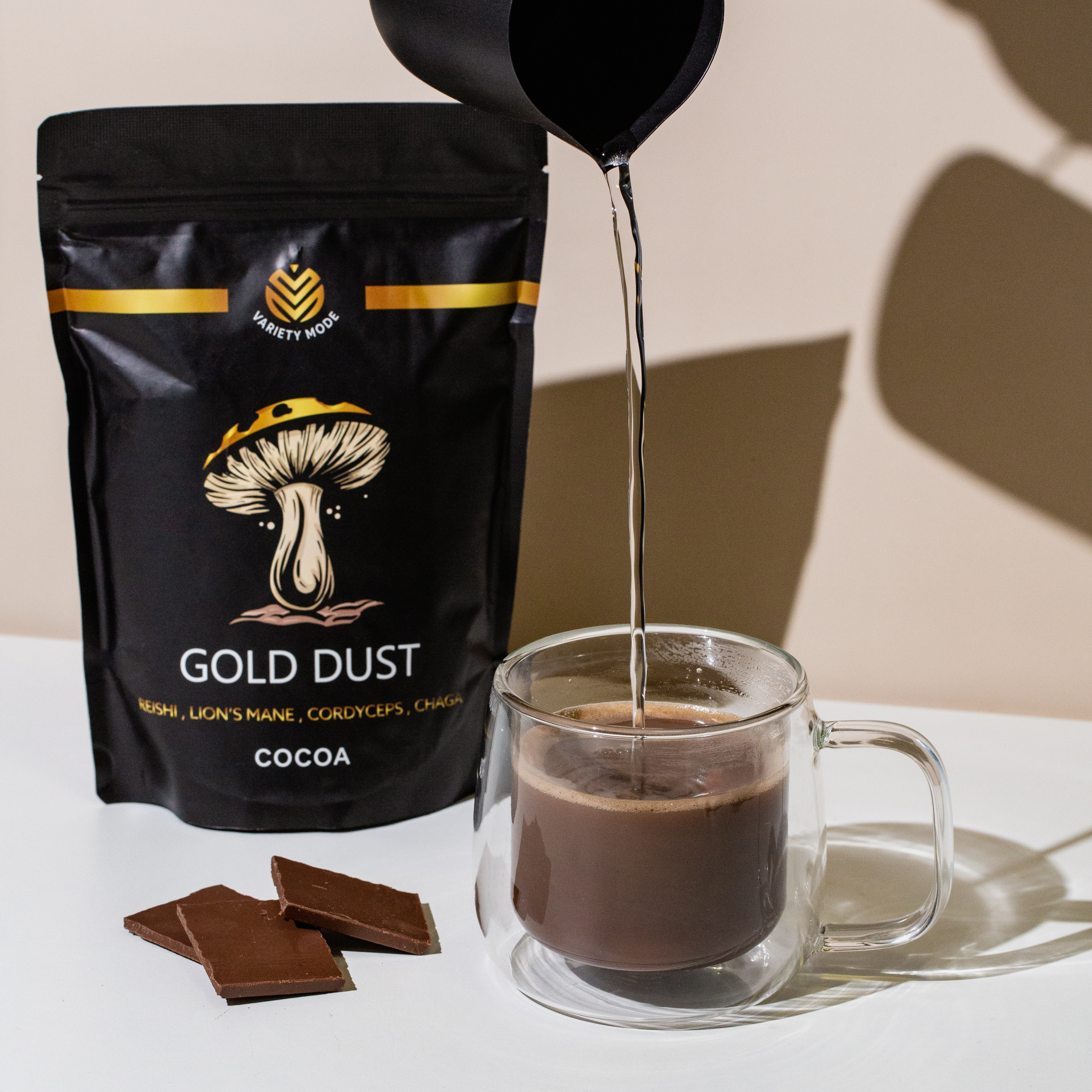 A bag of cocoa powder, chocolate pieces, and a glass mug being filled with liquid.