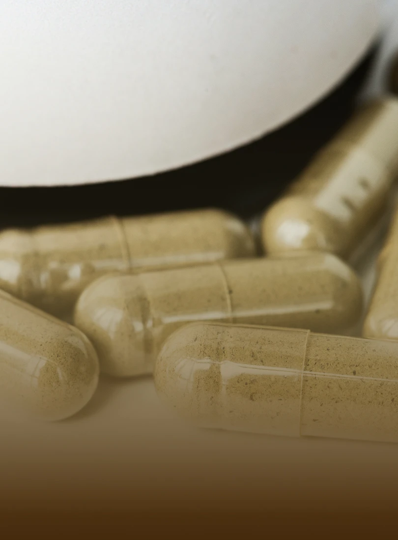 A close-up shot of several translucent capsules filled with a tan powder next to a white bottle.