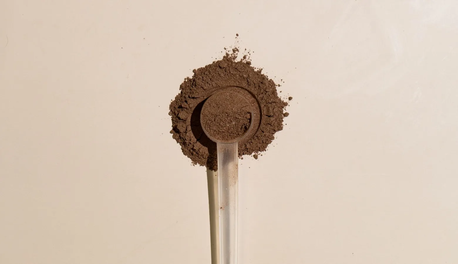 A top-down view of a clear plastic scoop filled with brown powder, resting on a small pile.