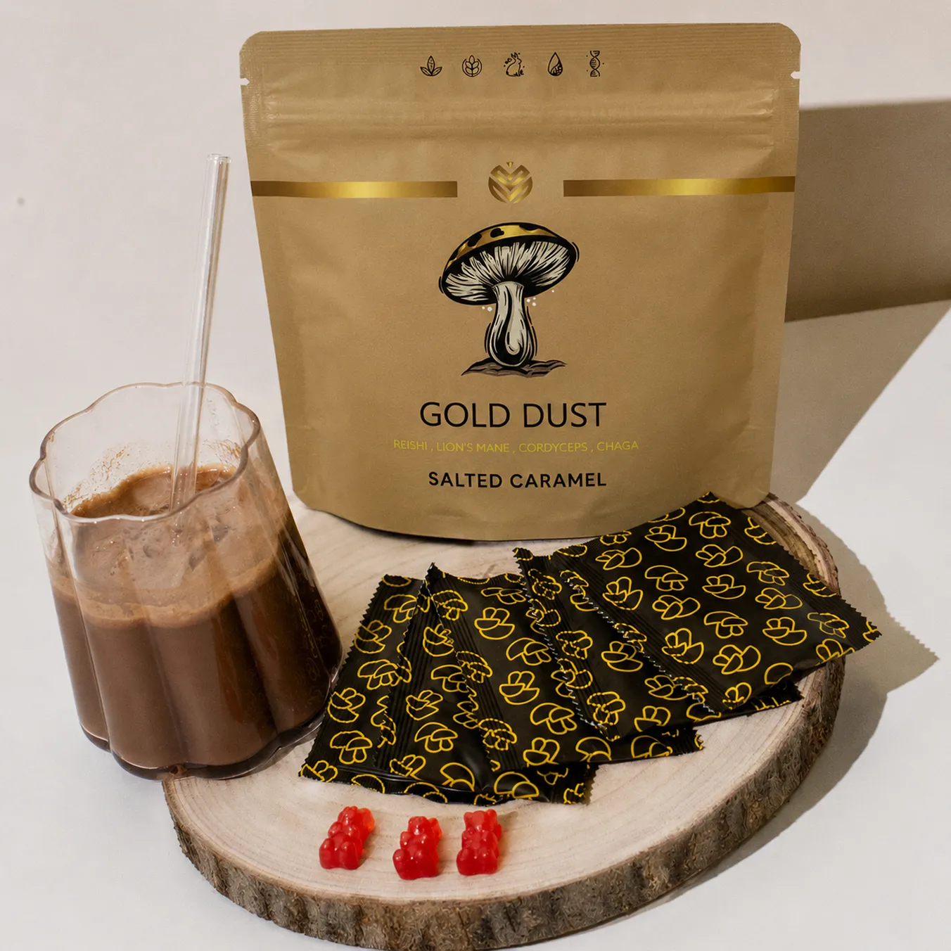 A bag of Gold Dust mushroom powder next to a drink, individual packets, and three red gummy bears.