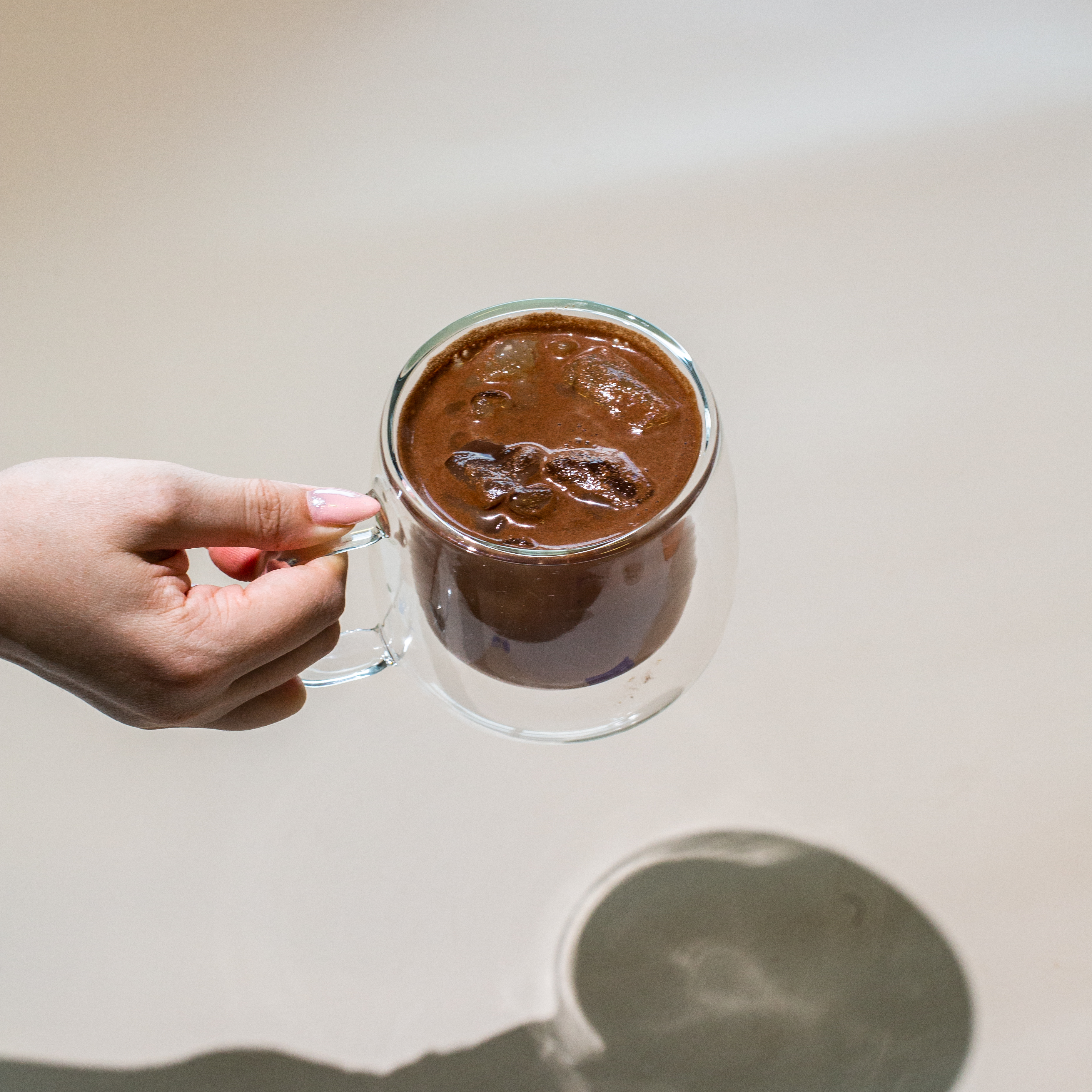 Hand holding a glass mug of iced chocolate drink.