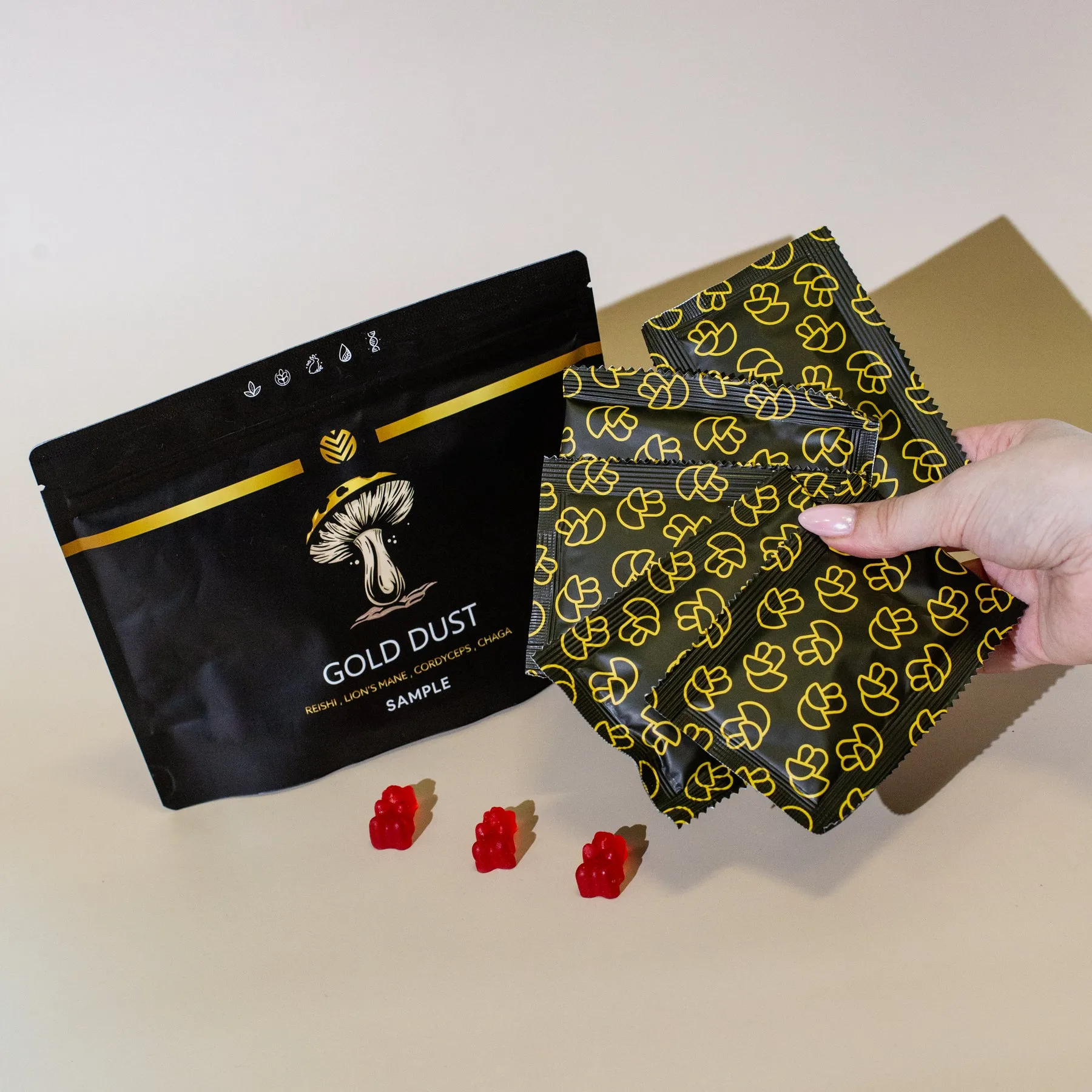 A hand holds packets of mushroom gummies next to a larger sample pouch and three red gummies.