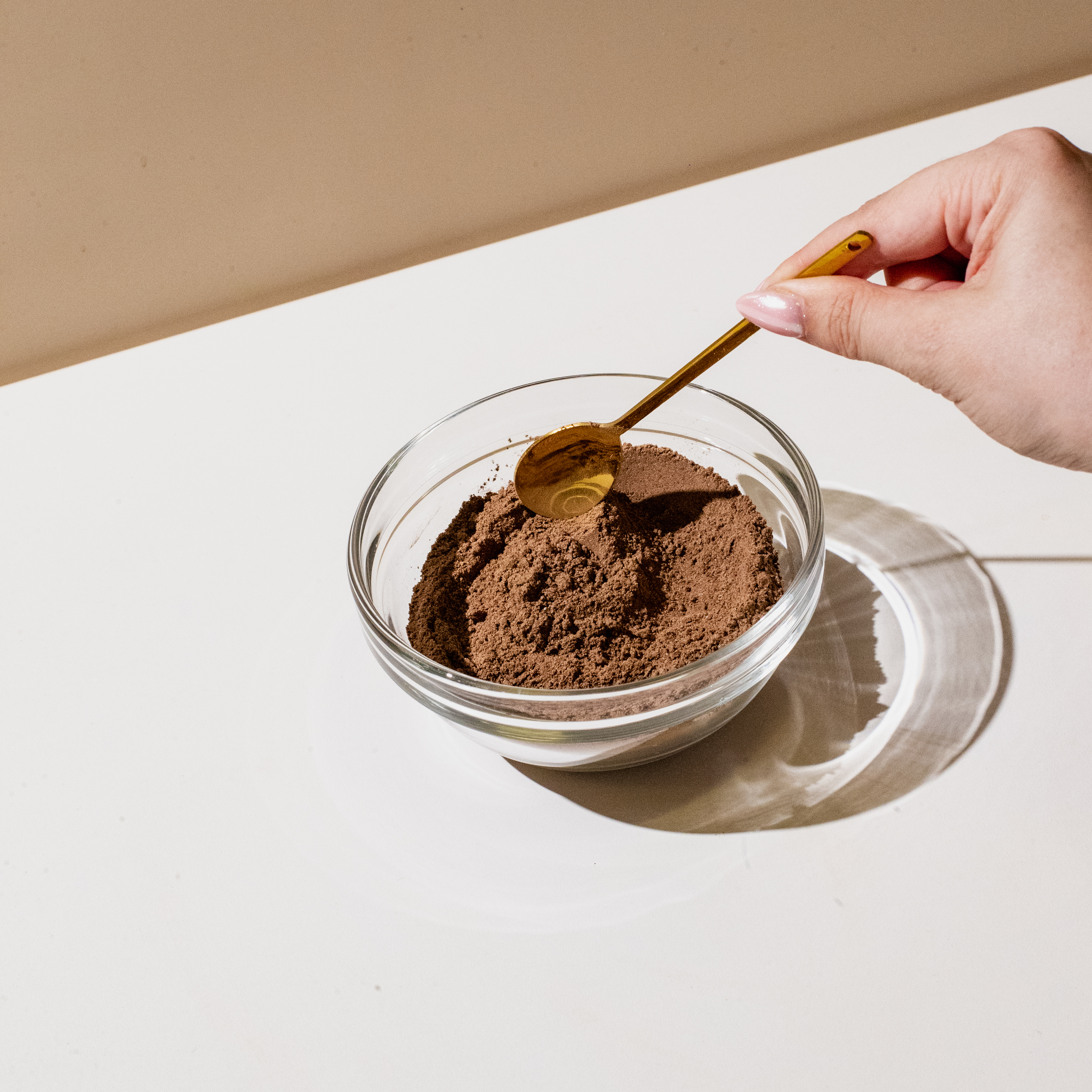 Hand holding a spoon over a bowl of cocoa powder.