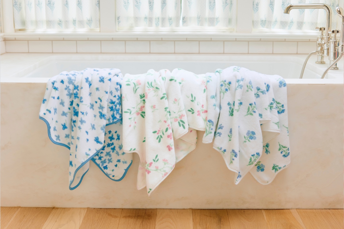 Three floral-patterned towels draped over a bathtub edge.