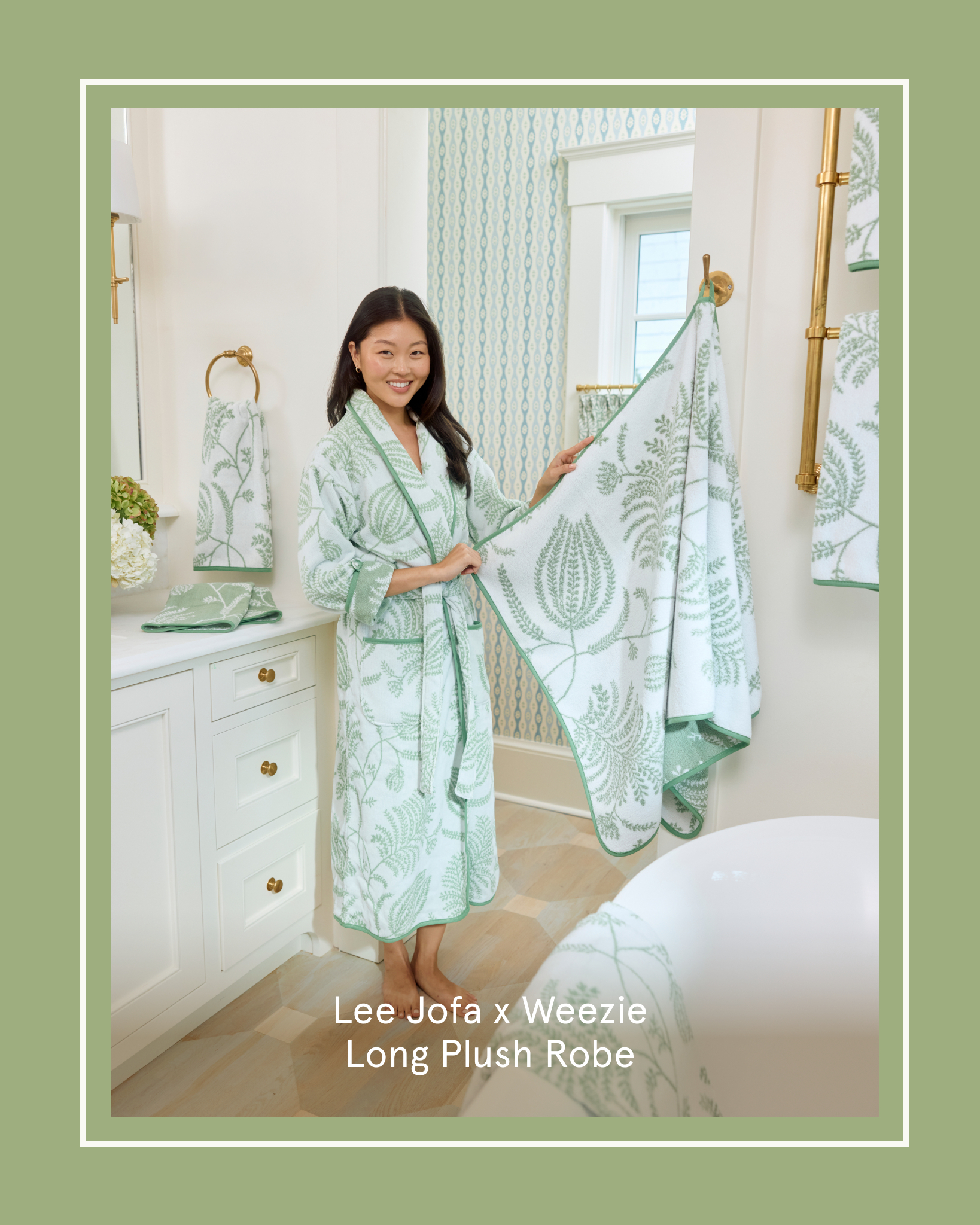 A woman in a white and green patterned robe holds up a matching towel in a bathroom.