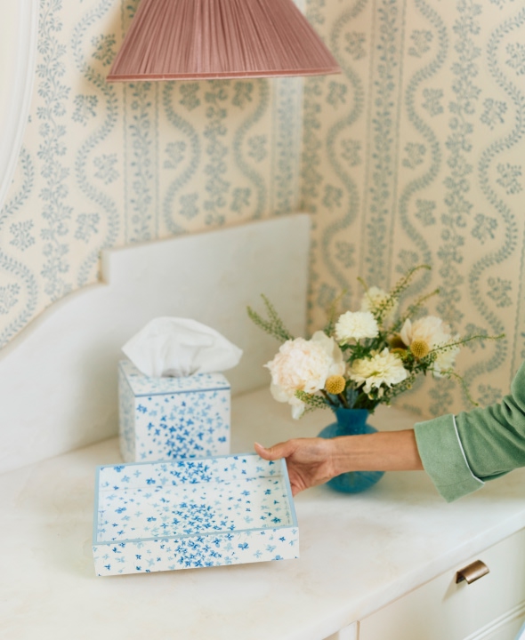 Hand reaching for a blue floral box on a counter with flowers and tissues.