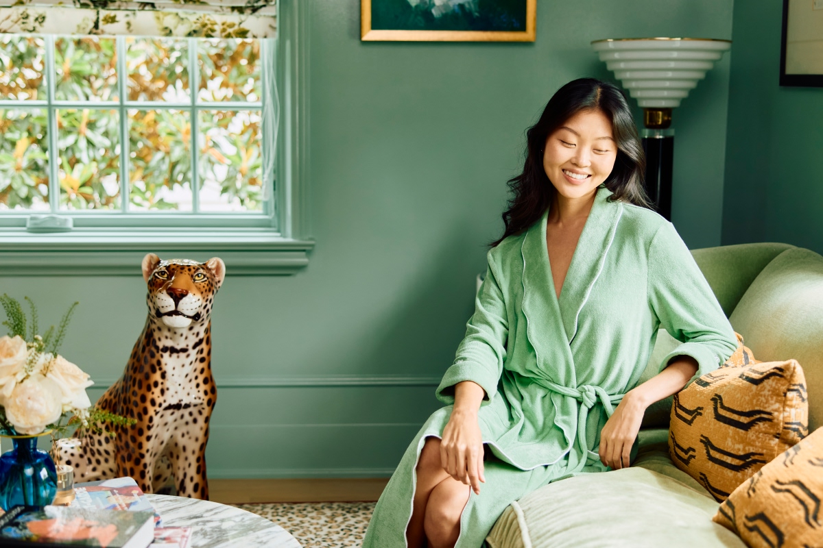 Woman in green robe sitting on a couch with a leopard statue nearby.