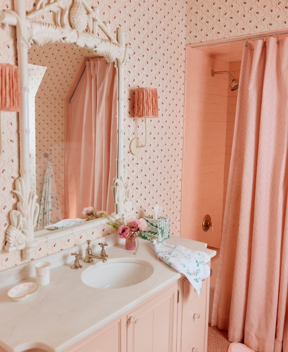 Vintage-style bathroom with pink decor, floral wallpaper, and a mirror above the sink.