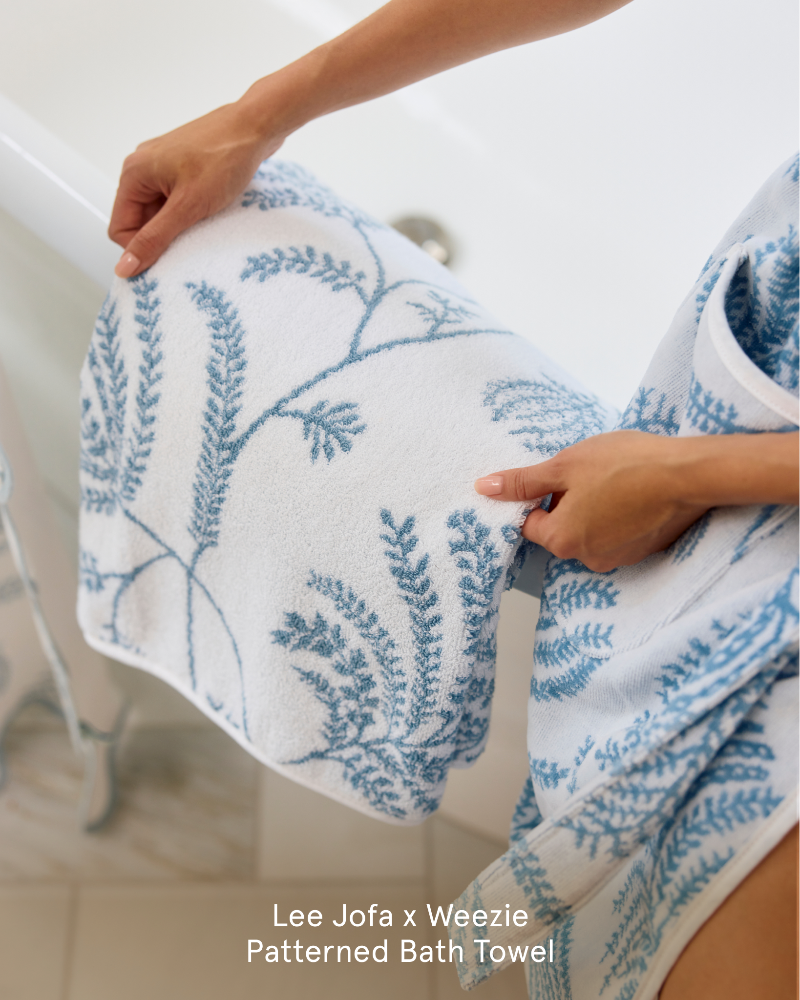 A person holds a white towel with a blue botanical pattern over the side of a bathtub.