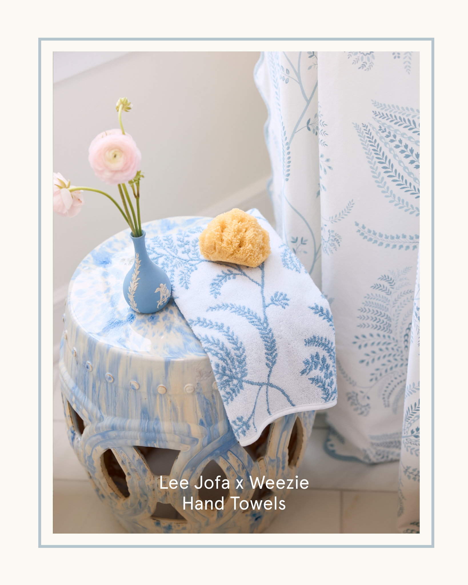 A blue patterned hand towel on a ceramic stool with a vase of flowers and a sea sponge.