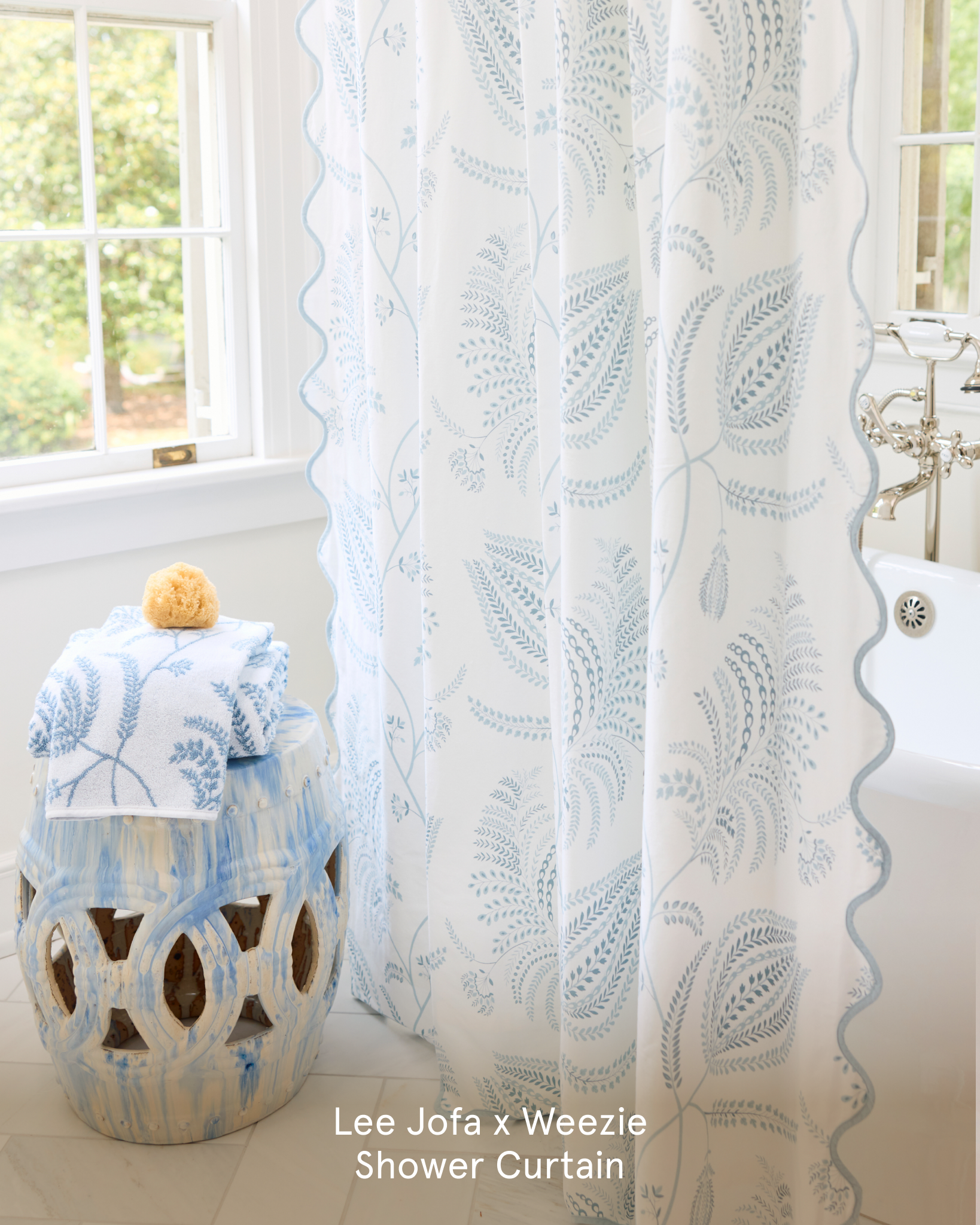A white shower curtain with a blue botanical print hangs next to a tub and matching towels.