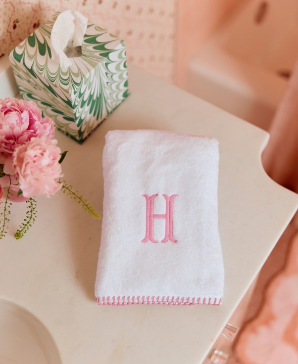 White towel with pink 'H', pink flowers, and tissue box on a bathroom counter.