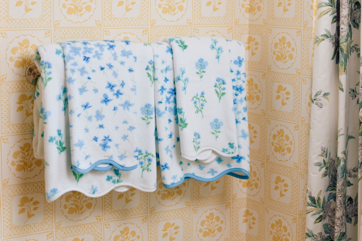 Two floral towels hanging on a patterned bathroom wall.