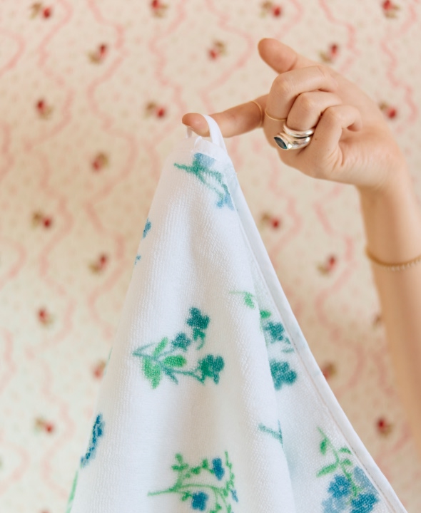 Hand holding a floral-patterned towel against a patterned wallpaper background.