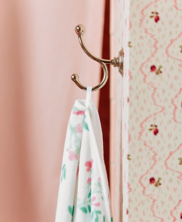 Floral towel hanging on a brass hook against a patterned wall.