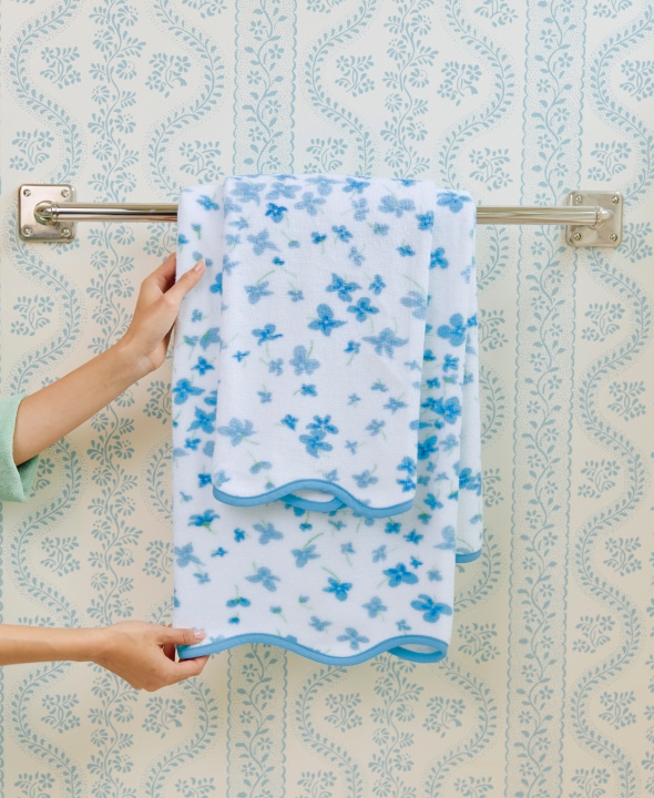 Hands adjusting a blue floral towel on a rack against patterned wallpaper.