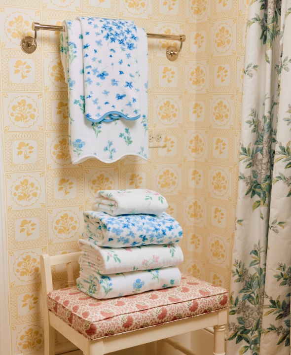 Stack of floral towels on a chair in a patterned bathroom.