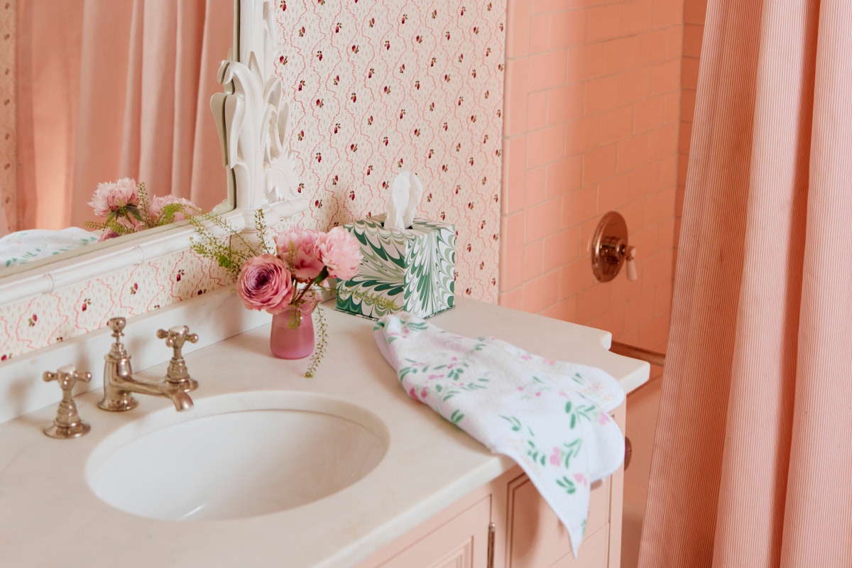 Pink bathroom with floral wallpaper, sink, flowers, and a tissue box.