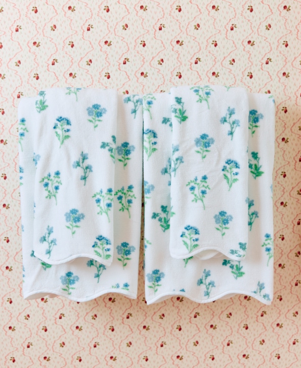 Two white towels with blue floral patterns hanging on a patterned wall.