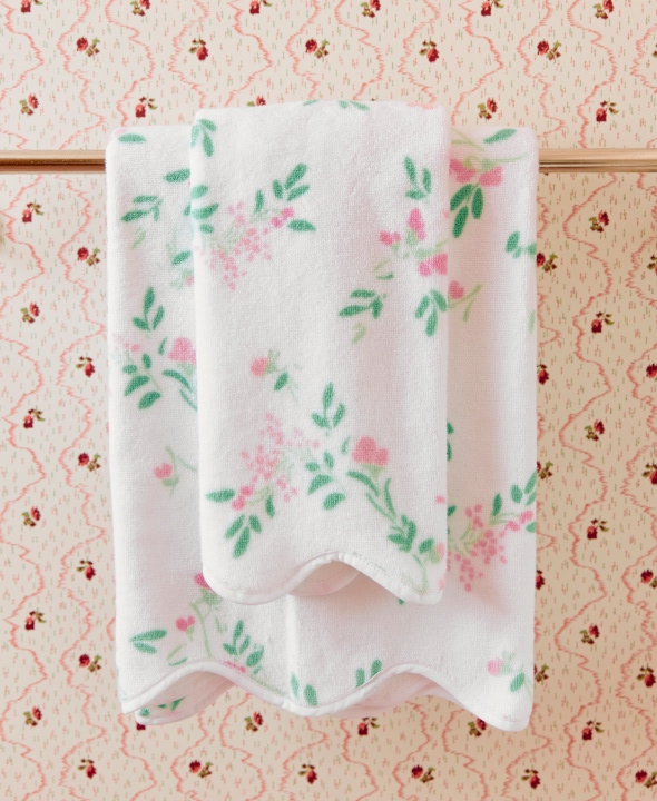 Floral-patterned towel hanging on a rod against floral wallpaper.