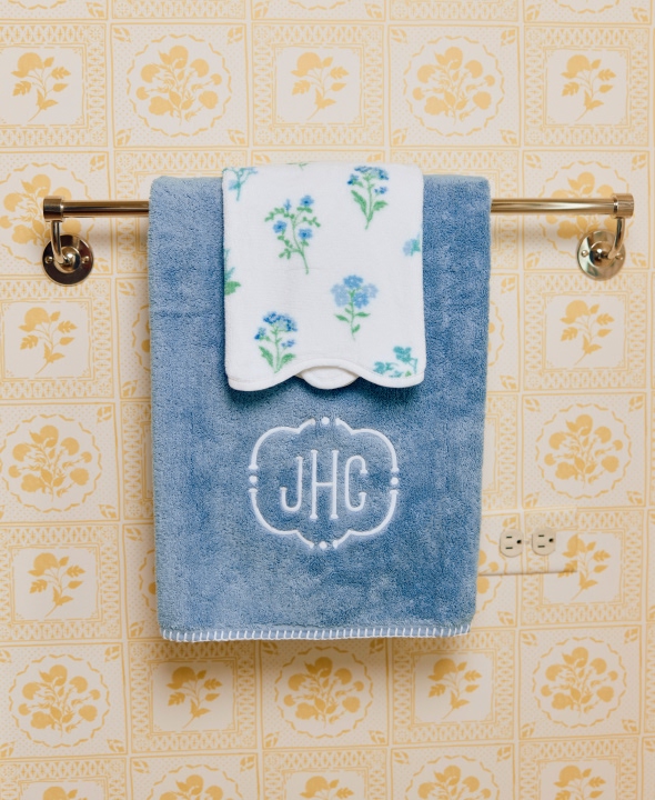 Blue towel with monogram 'JHC' and floral cloth on a towel rack.