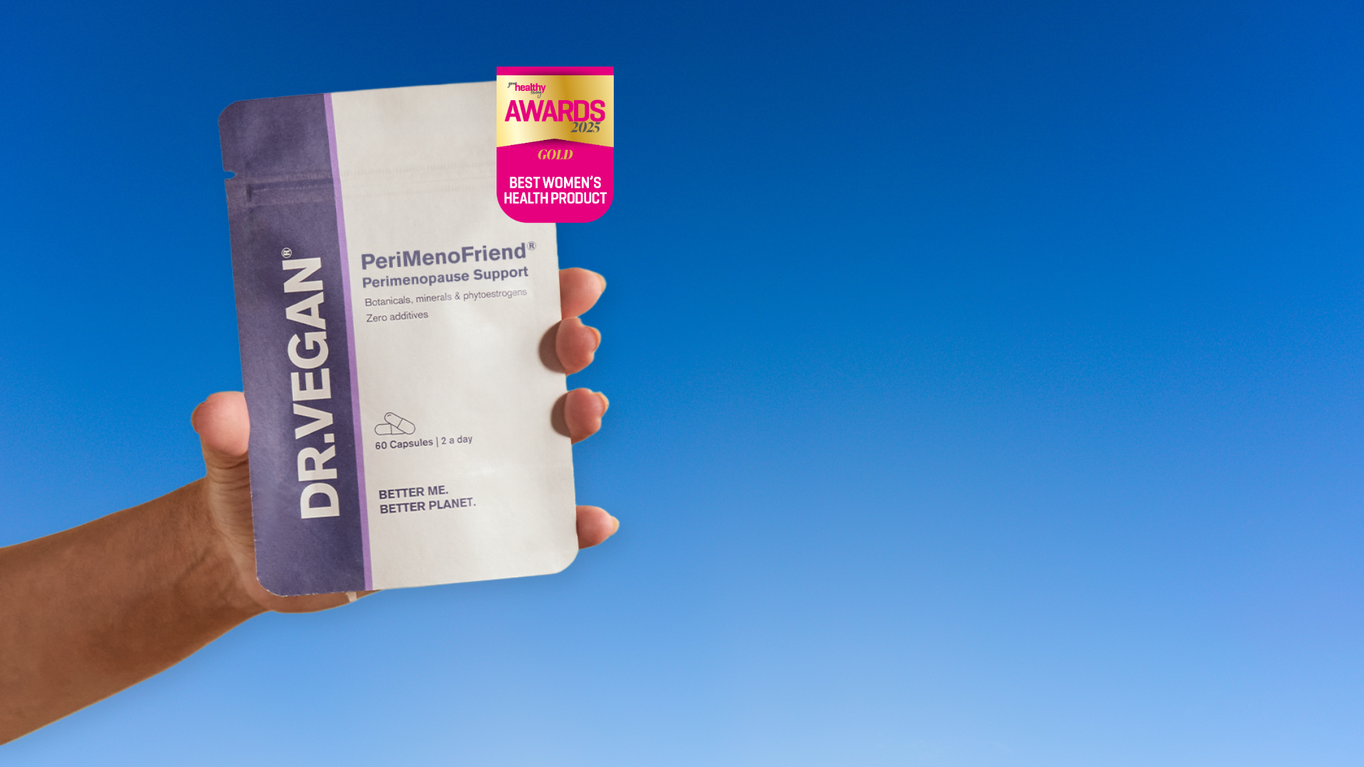 Hand holding a DR.VEGAN supplement packet against a clear blue sky.
