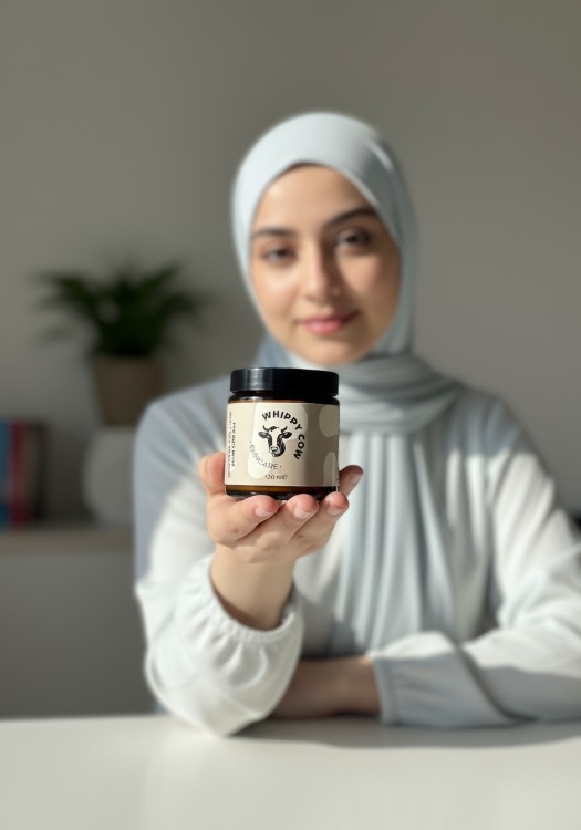 Person smiling, holding a jar, indoors with plants and frames in the background.