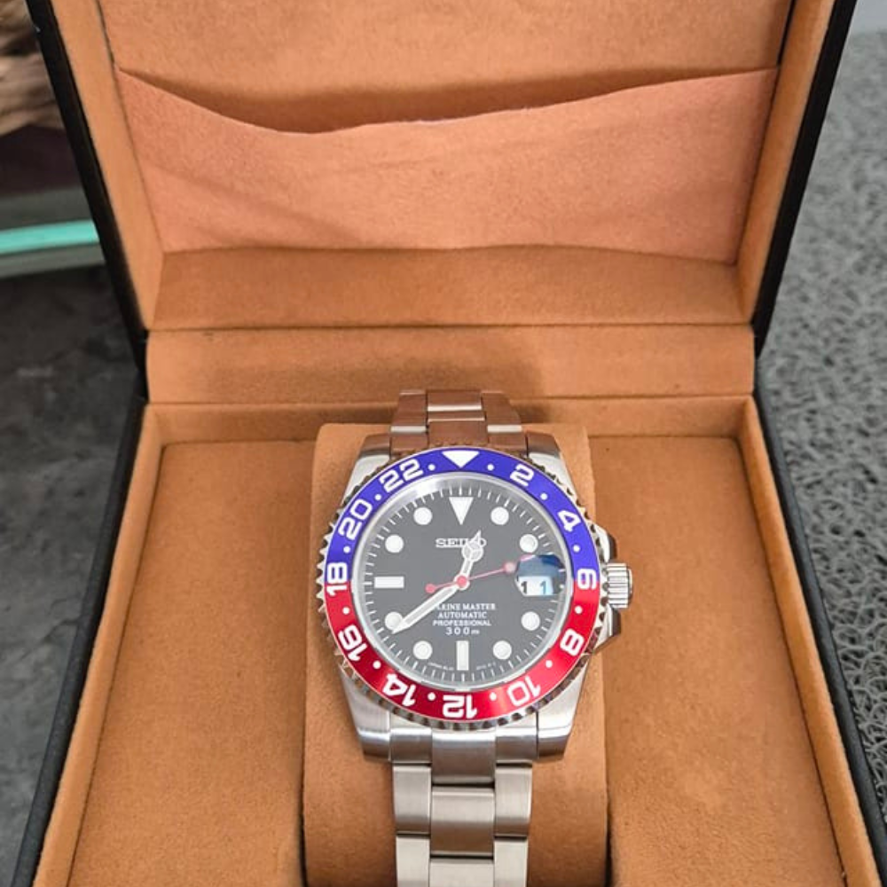 Stainless steel watch with a red and blue bezel in a tan display box.