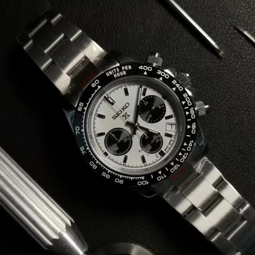Silver chronograph watch with a white face and black bezel, displayed on a dark surface.