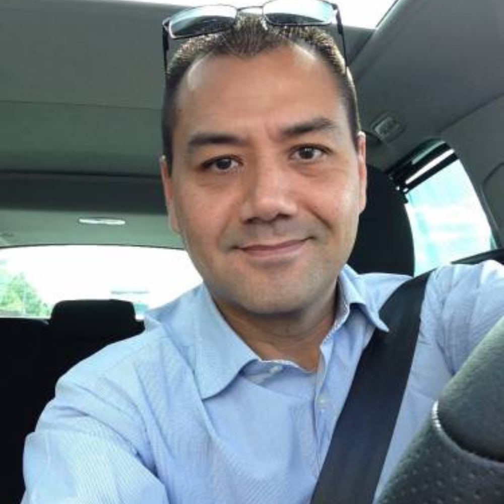 Man smiling while sitting in a car, wearing a blue shirt.