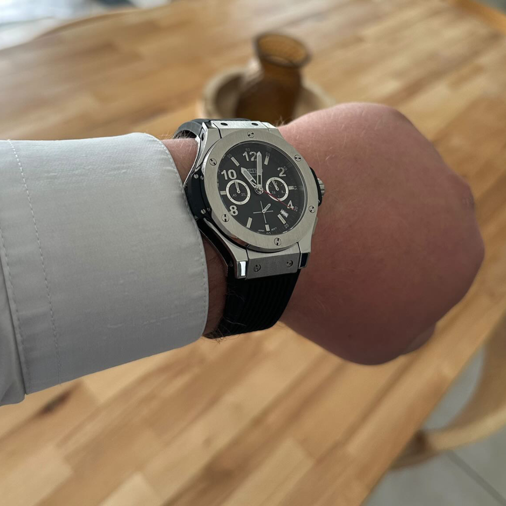 A person wearing a silver, large dial watch with a black strap.