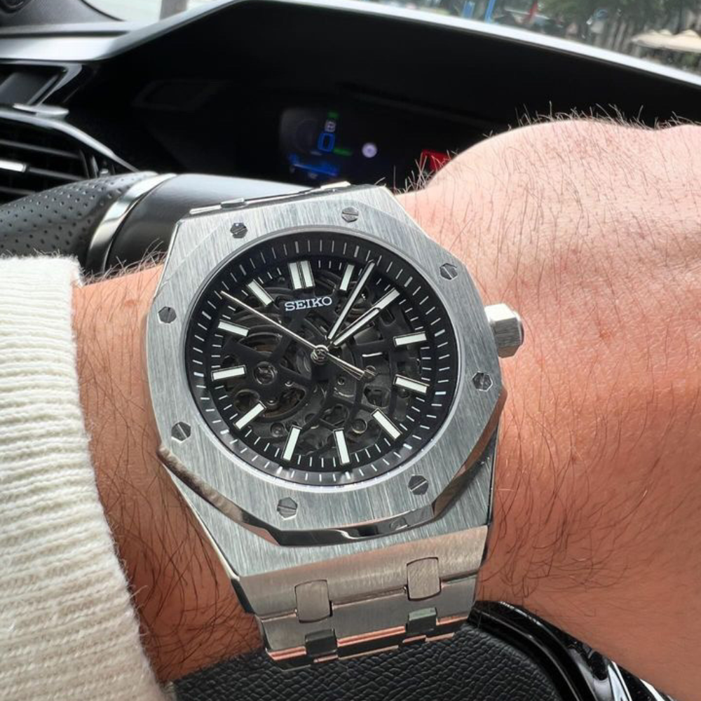 Stainless steel Seiko wristwatch with a skeleton dial on a person's wrist inside a car.