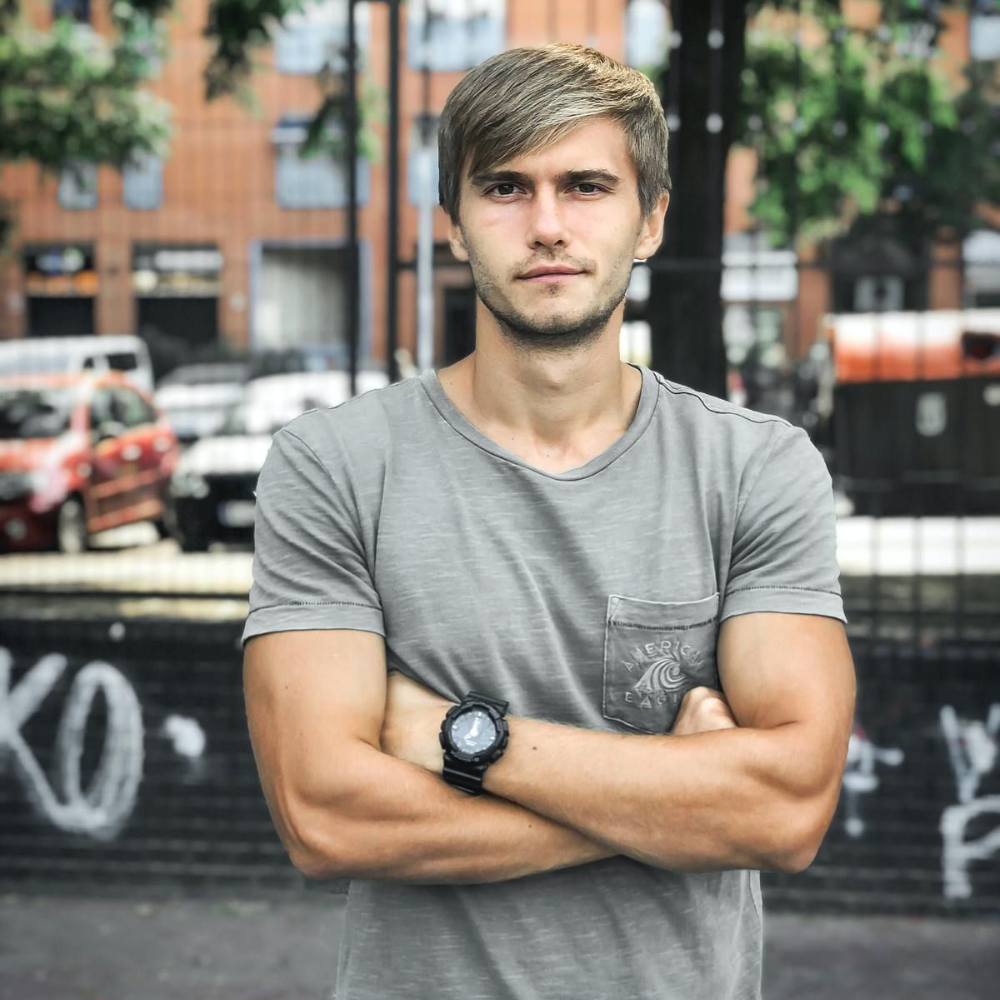 Man in a gray t-shirt with crossed arms, standing outdoors.