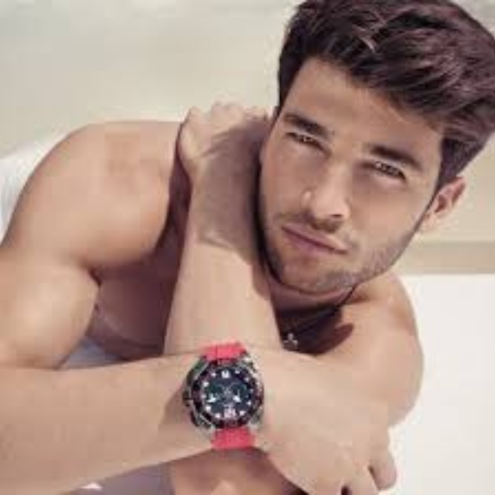 Man with short hair and a red watch, resting his arm on a surface.
