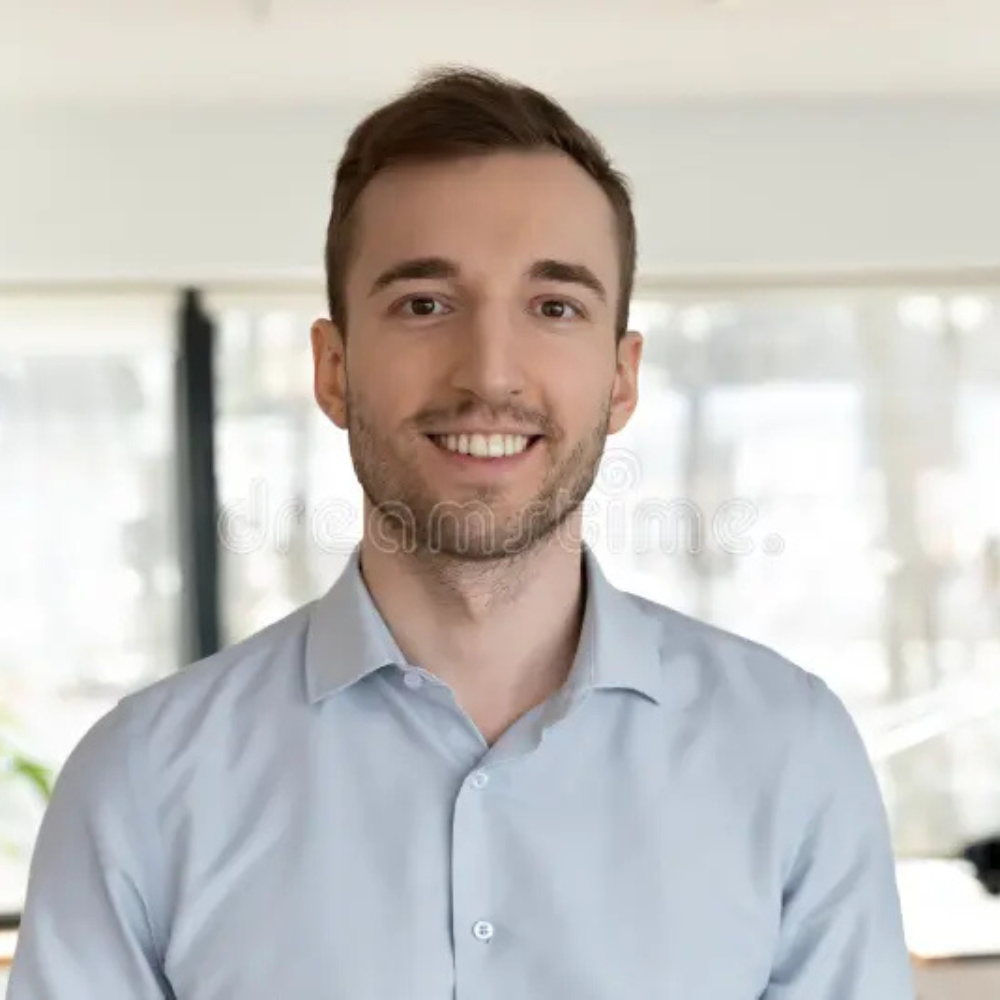 Smiling person in a light blue shirt against a bright, out-of-focus background.